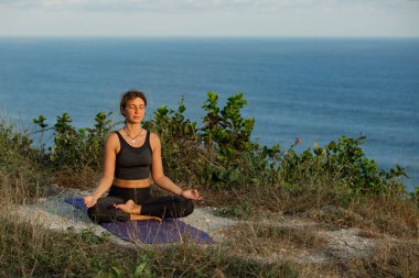 Deniz kıyısında lotus pozisyonunda meditasyon yapan genç bir kadın.