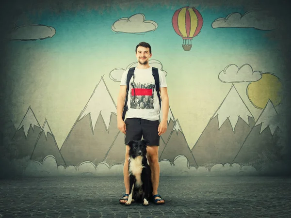 Happy guy carrying a backpack and his border collie dog dream of holiday trip isolated on grey wall with drawn mountains and hot air balloon. Friendship between man and pet starting the new adventure.