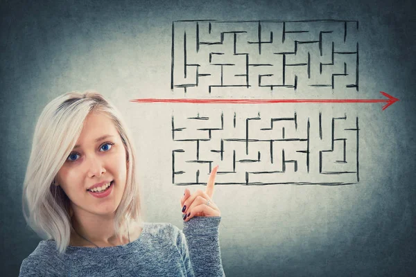 Close up portrait of a puzzled woman pointing her finger up showing a solution to escape from labyrinth. Young businesswoman breaking the rules, as a red line pierce the maze walls.
