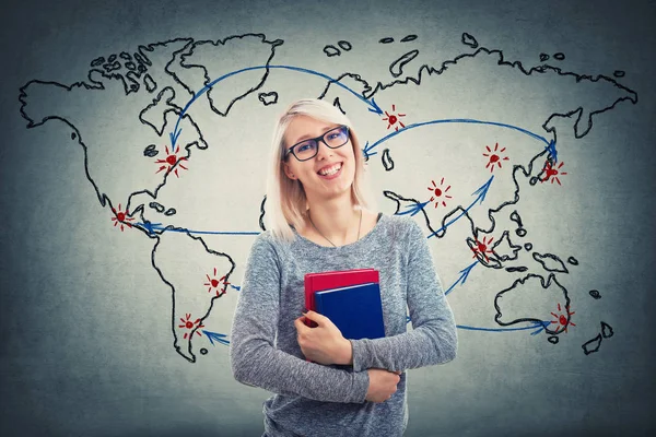 Young woman wearing glasses and holding two books over world map background. Global education concept. Cheerful student girl planning her next point on map to continue studying.