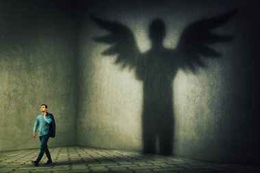 Proud and confident young businessman casting a superhero shadow with angel wings on a dark room wall. Inner power, ambition and leadership concept. clipart