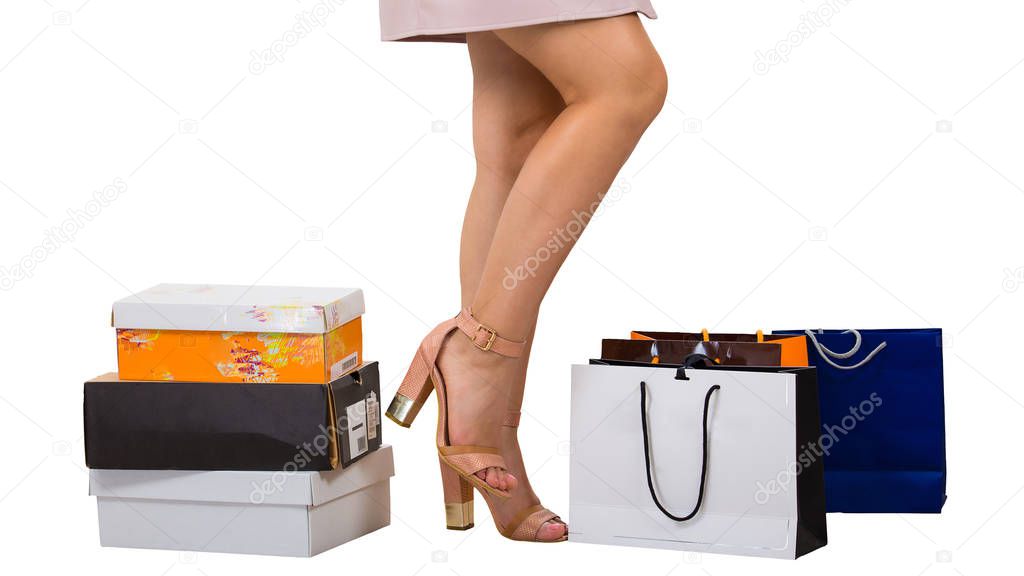 Close up of female legs wearing high heel shoes and shopping bags and boxes isolated over white background.