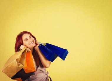 Holding alışveriş torbaları ararken ve kopya alanı ile sarı arka plan üzerinde izole rüya yanakları için eller güzel jouyful genç kadın.