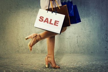 Yan görünümü bir sürü kağıt poşet ve beton duvar arka plan üzerinde izole hediyeler taşıyan alışveriş sonra yürüyüş kadın bacak kadar kapatın.