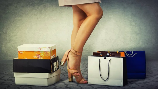 Close up of female legs wearing high heel shoes and shopping bags and boxes isolated over grey wall background.