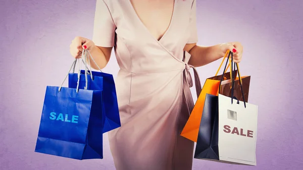 Close up of a woman body waist with hands holding shopping bags isolated over purple background. Holiday sale season.