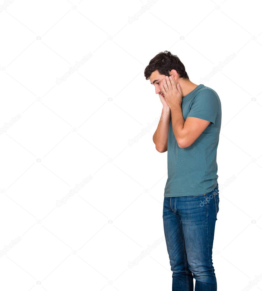 Side view of a disappointed and stressed young man hands on cheeks looking down isolated over white background with copy space. Sad feeling, negative human emotion.