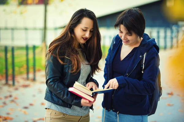 两位开朗的年轻女学生指指点点一本书 为她们的问题找到正确的答案 教育是解决生活问题的办法 团队合作和友谊理念 — 图库照片