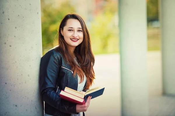 在大学校园里抱着一本打开的书看相机户外微笑的年轻妇女学生 — 图库照片