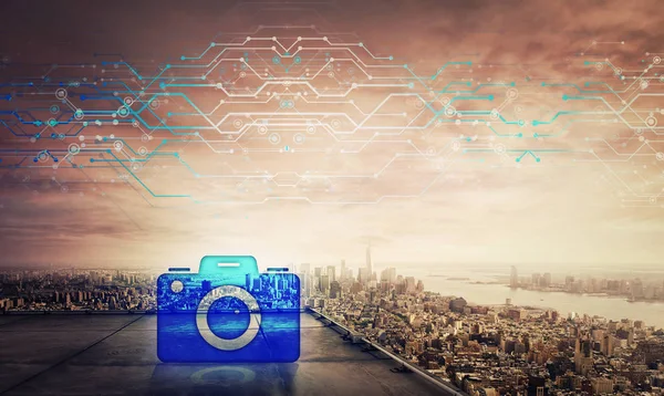 Blue professional camera icon hologram on the rooftop of a skyscraper over the big city sunset horizon, double exposure effect. Modern technology in photography. Virtual business services.