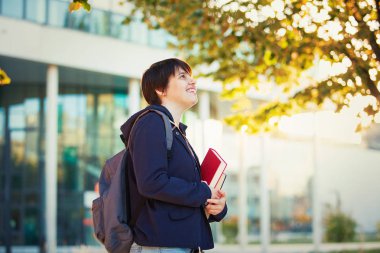 Mutlu genç kadın öğrenci holding kitap ve sırt çantası açık havada Üniversitesi Kampüs portre sezon sonbahar. Yaşam tarzı eğitim kavramı.