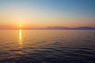 Muhteşem deniz günbatımı sakin su ve ufukta sisli tepeler ile.