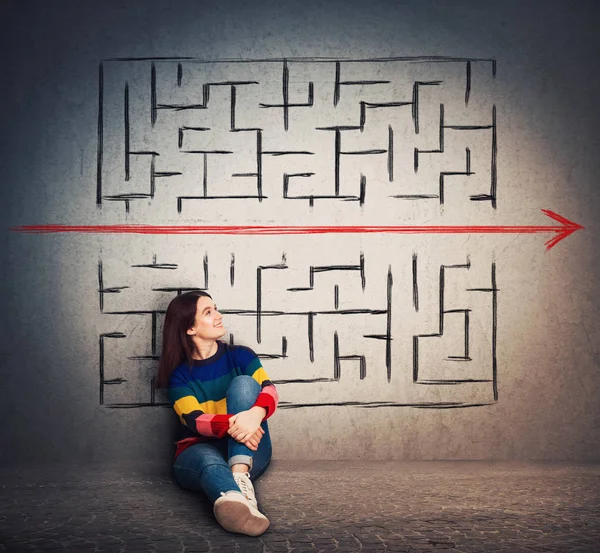 Casual young woman sitting on the floor finding a solution to solve problem and escape from labyrinth. Breaking the rules, as a red arrow pierce the maze walls. Different thinking, alternative idea.