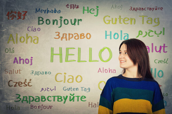 Pretty girl in front of a blackboard written with the word hello in different languages and colors. Opportunity for learning many languages for students.
