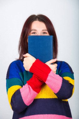 Gri arka plan üzerinde izole bir kitap arkasına saklanmış utangaç kadın öğrenci.