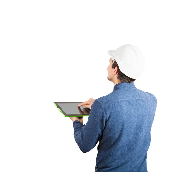 タブレット コンピューターのガジェットを使用して コピー領域と白い背景上分離見上げてを計算する保護ヘルメットを身に着けている若手エンジニアの背面図 — ストック写真