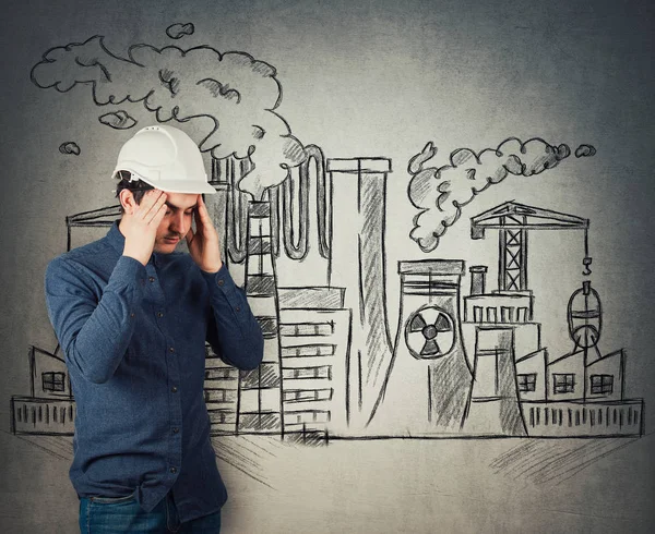 Stressed young man engineer industry worker holding arms to head feeling exhausted. Headache and health problems. Toxic factory sketch, nuclear plants emit smoke. Dirty, contaminated air pollution.