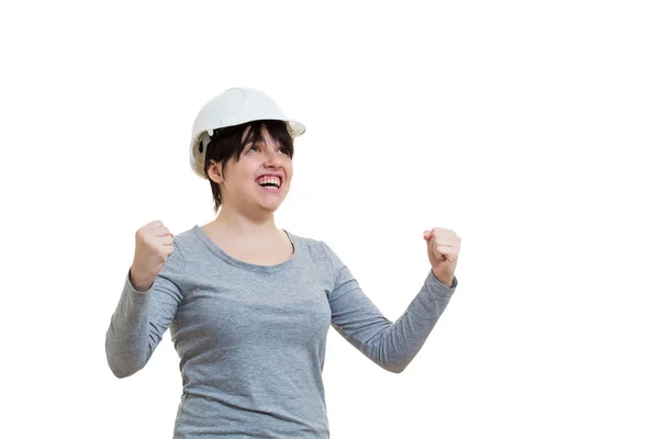 コピー スペースで白い背景に分離成功を祝う見上げて手を上げる拳を抱きしめて保護ヘルメットを身に着けている興奮した若い女性エンジニア — ストック写真