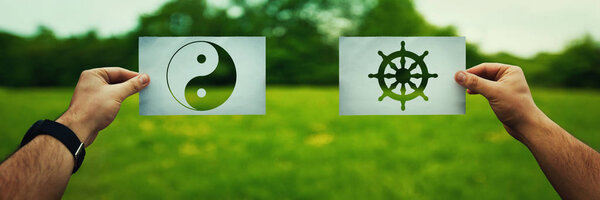 Religion conflicts as global issue concept. Two hands holding different faith symbols of China, Buddhism vs Taoism belief over green field nature. Relations between different people doctrines and cult