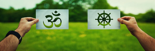 Religion conflicts as global issue concept. Two hands holding different faith symbols, Buddhism vs Hinduism belief over green field nature. Relations between different people doctrines and cult.