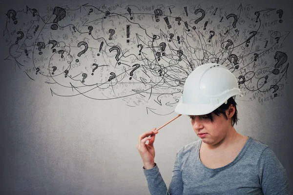 Thoughtful young woman engineer wearing protective helmet thinking pointing pencil to head, stressed looking down feeling exhausted. Headache, anxiety and health problems as sketch mess in his head.