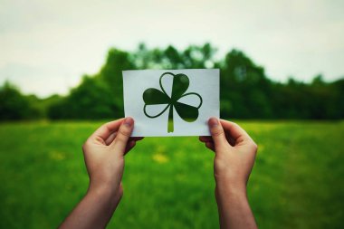 St Patricks Günü, yonca sembolü ile bir kağıt levha yeşil alan doğa arka plan üzerinde tutan el olarak şans muskaları. Bahar İrlandalı tatil kutlaması, shamrock simgesi.