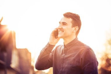 Gün batımında açık havada cep telefonu ile Gülümseyen Genç Adam