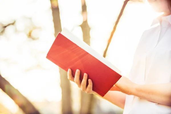 Studente ragazza all'aperto tenendo un libro rosso su sfondo soleggiato — Foto Stock