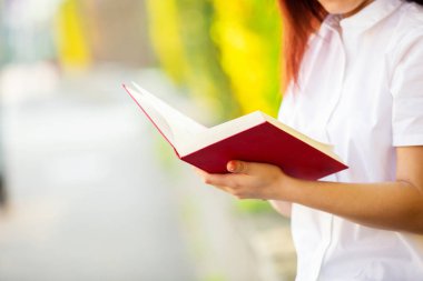 Güneşli arka plan üzerinde kırmızı bir kitap tutma