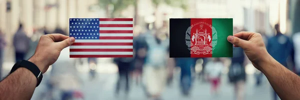 Two hands holding different flags, US vs Afghanistan on politics