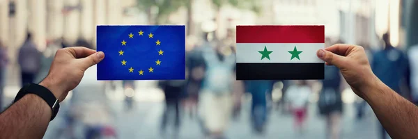 Two hands holding different flags, European Union vs Syria on po