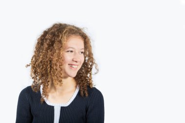 Kıvırcık saçlı mutlu genç kızın portresi gri arka plan üzerinde sol bakarak gülümseyen. Pretty kıvırcık kız gülümseyen ve bir şey arıyor.