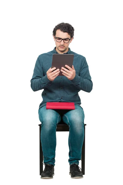 Ciekawy Uczeń Siedzący Krześle Używając Tabletu Trzymając Czerwoną Książkę Kolanach — Zdjęcie stockowe