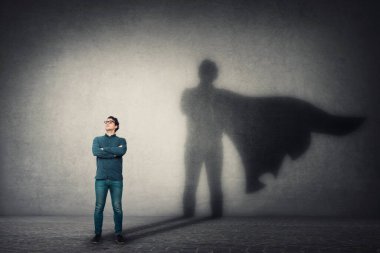 Cesur adam kollarını kavuşturur, kendinden emin görünür, duvarında pelerin gölgesi olan bir süper kahraman bırakır. Hırs ve iş başarısı konsepti. Liderlik kahraman gücü, motivasyon ve içsel güç sembolü..