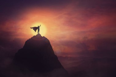 Kavramsal günbatımı sahnesi, bir dağın tepesinde cesur duran süper kahraman bir elini kazanan bir lider olarak kaldırmaya kararlı görünüyor. Kahraman güç ve motivasyon, engelleri aşmak.