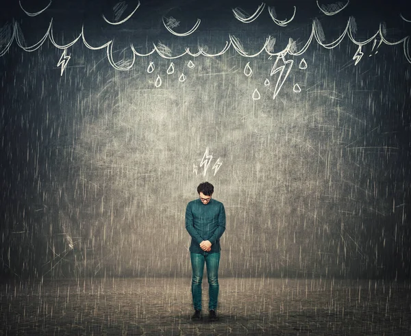 Human depression and emotional breakdown concept, as sad businessman looks down disappointed, has no umbrella protection while stands under the rain, thunderstorm as metaphor for mental health issues.