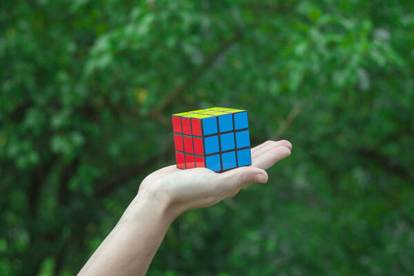 POIANA TEIULUI, ROMANIA - JULY 16, 2018: hand holding Rubik cube puzzle against a green tree background