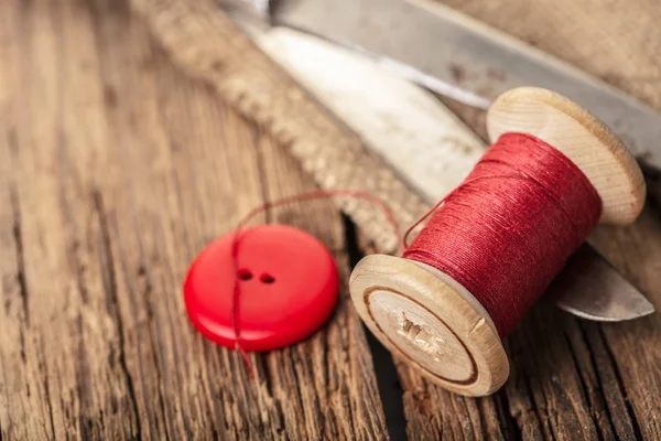 red thread with buttons and scissors, wooden background