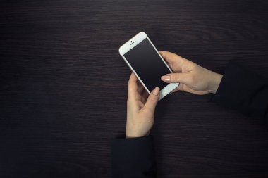 Ahşap bir arka planda kadın ellerinde cep telefonu.