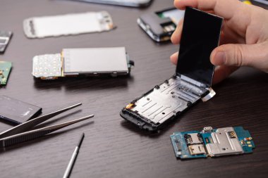 Cep telefonu tamiri, ahşap masaya yakın duran eller.