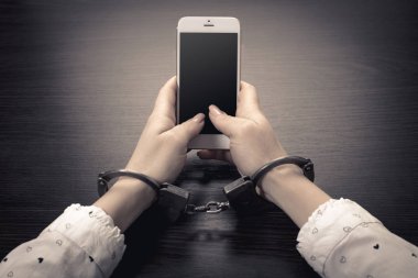 Elleri kelepçeli, ahşap arka planda cep telefonu var.