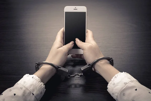 木製の背景に携帯電話で手錠をかけられた手 — ストック写真