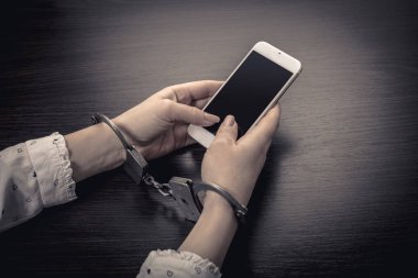 Elleri kelepçeli, ahşap arka planda cep telefonu var.