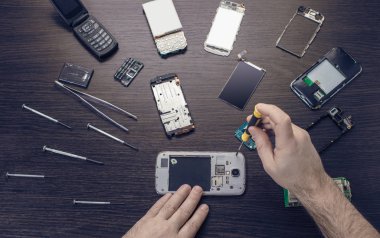 Cep telefonu tamiri, ahşap masaya yakın duran eller.