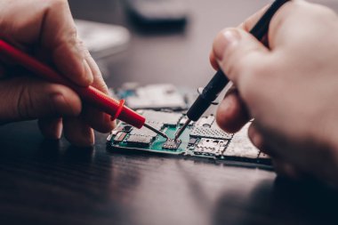 Cep telefonu tamiri, ahşap masaya yakın duran eller.