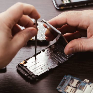 Cep telefonu tamiri, ahşap masaya yakın duran eller.