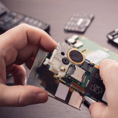 Cep telefonu tamiri, ahşap masaya yakın duran eller.