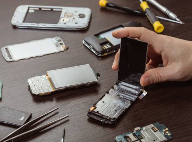 Cep telefonu tamiri, ahşap masaya yakın duran eller.