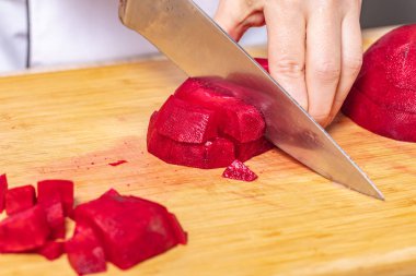 Aşçı, ahşap bir tahtanın üzerinde kırmızı pancar keser, yemek pişirmeye hazırlanır.