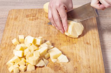 Aşçı patatesleri ahşap bir tahtada keser, yemek hazırlar.